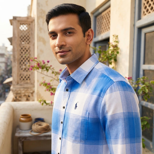 A South Asian man wearing a blue and white check shirt in a sunlit urban setting, highlighting the lightweight fabric.