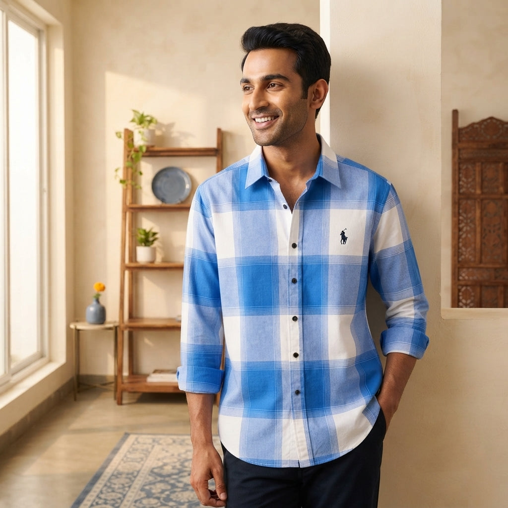 A South Asian man wearing a blue and white check shirt in a bright, modern living room.